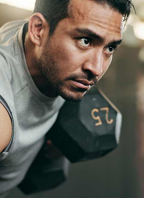A man in a grey tank top is doing push-ups in a gym.
