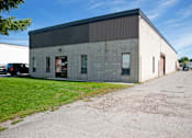 Thumbnail 1 of 4 - A large industrial building with a grey and white exterior and a parking lot in front.