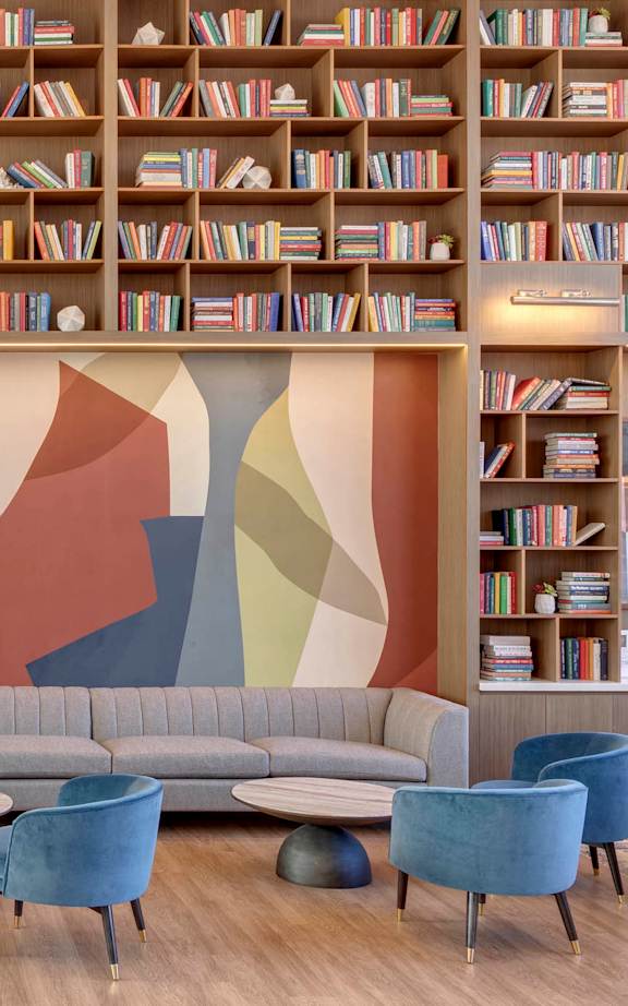A living room with a grey sofa, blue chairs and a bookshelf filled with books.