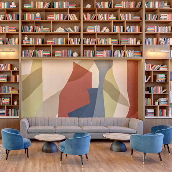 A living room with a grey sofa, blue chairs and a bookshelf filled with books.