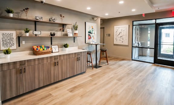 Modern apartment lobby with wood flooring, built-in cabinetry, floating shelves, and welcome snack display at Panton Mill Apartments