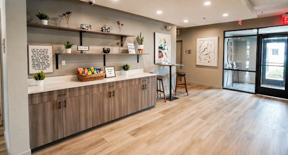 Modern apartment lobby with wood flooring, built-in cabinetry, floating shelves, and welcome snack display at Panton Mill Apartments