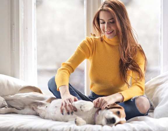 a woman sitting on a bed playing with her dog at Hampton in Highland Apartments, Indiana, 46322
