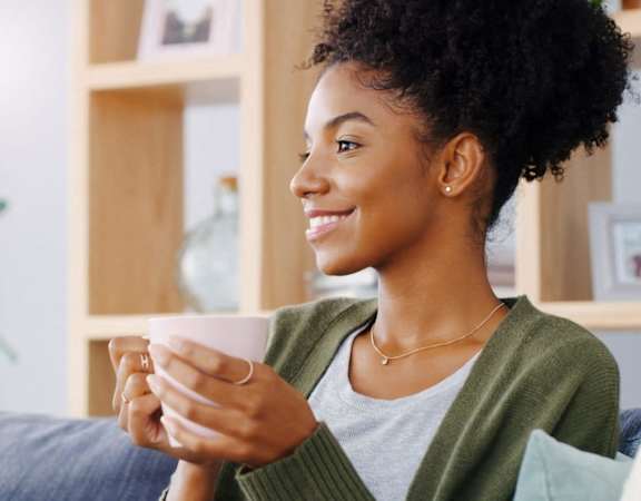a woman sitting on a couch holding a cup of coffee at Whitcomb Terrace Apartments, Merrillville, IN