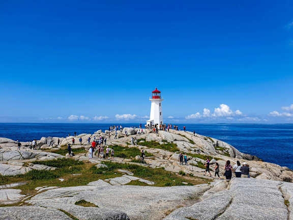 A white lighthouse with a red top stands on a rocky shore.