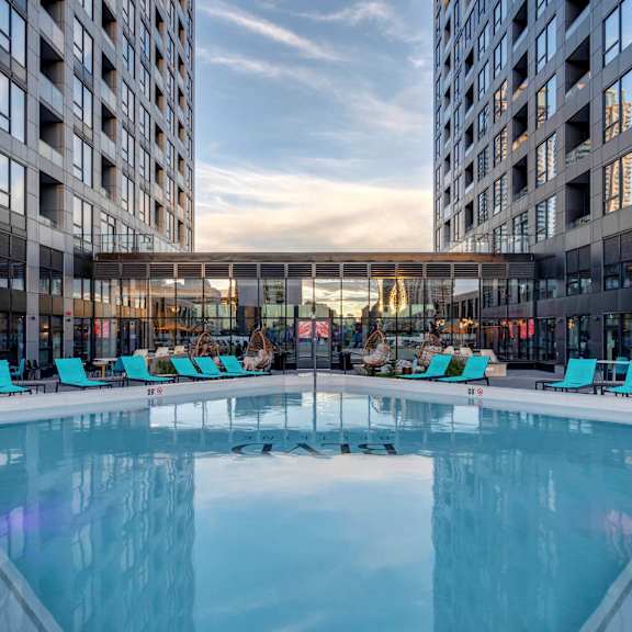 A large indoor swimming pool with lounge chairs is surrounded by two tall buildings.