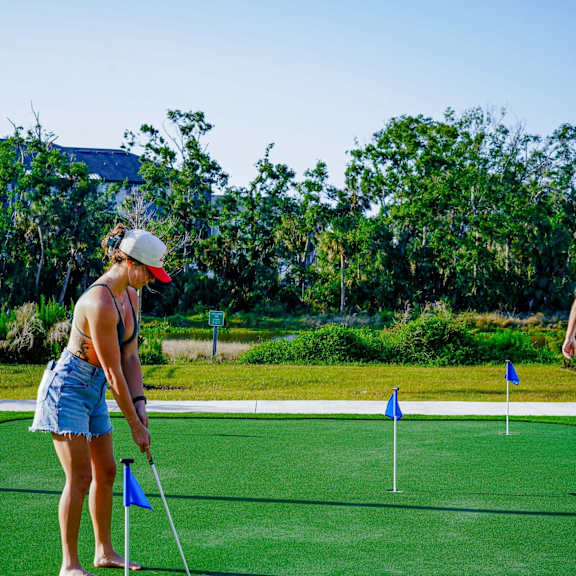 A woman is playing mini golf on a sunny day.