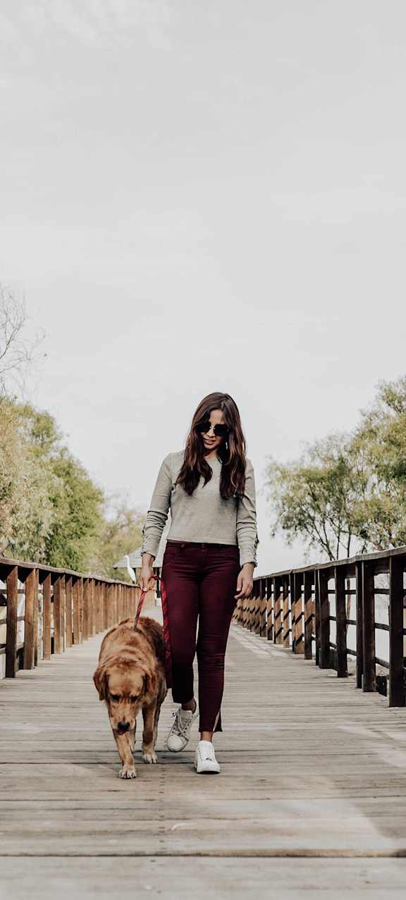 A woman walking a dog on a wooden bridge.