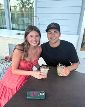 A man and a woman are sitting at a table with drinks and a green placard that says "TC".