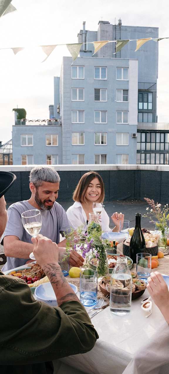 A group of people are enjoying a meal together at a table with a cityscape in the background.