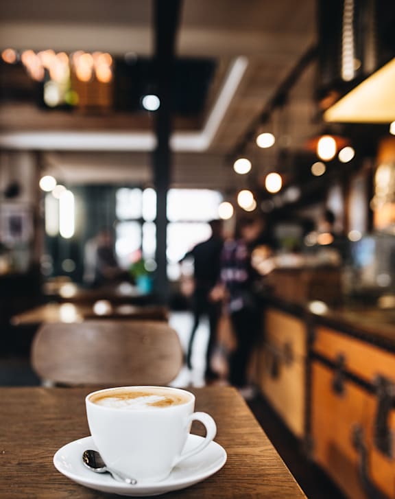 A cup of coffee with milk on a saucer on a wooden table in a cafe.