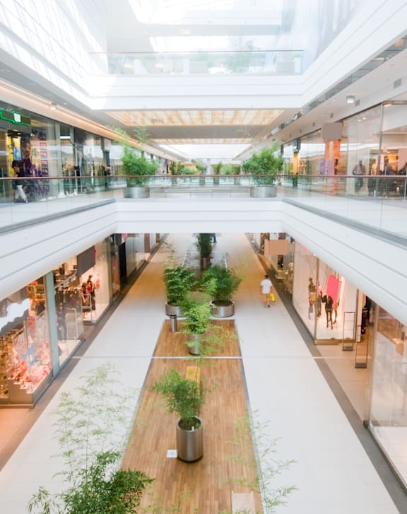 A long wooden table with plants on it in the middle of a shopping mall.