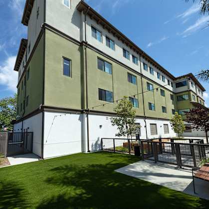 A modern building with a white and green exterior and a small courtyard in front.
