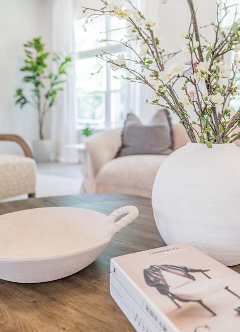 A white vase with branches in it sits on a table in a living room.