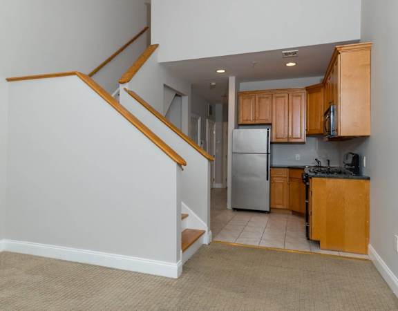A kitchen with a refrigerator, microwave, and oven is visible from the stairs.