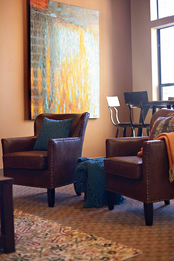 a living room with leather chairs and a painting on the wall