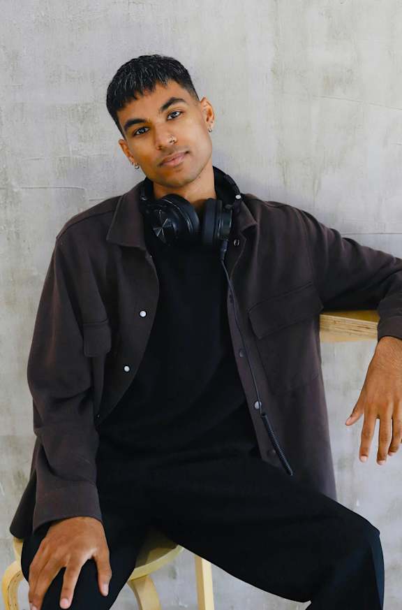 A person in a black shirt and pants is sitting on a chair with headphones around their neck.