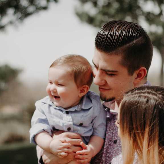 A man and woman hold a baby while standing outdoors.