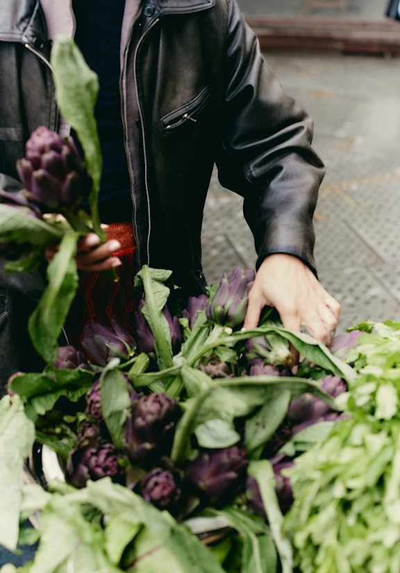 A person in a black jacket is holding a bunch of purple and green vegetables.