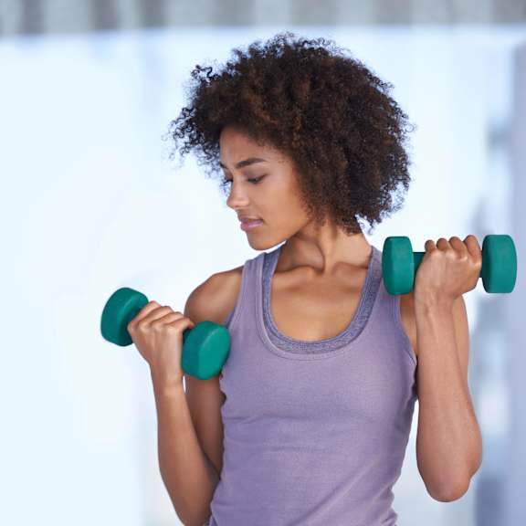 A woman with curly hair is lifting two green dumbbells.