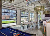 Thumbnail 4 of 8 - A pool table with a blue felt cloth and a set of pool balls in a room with a high ceiling and large windows.