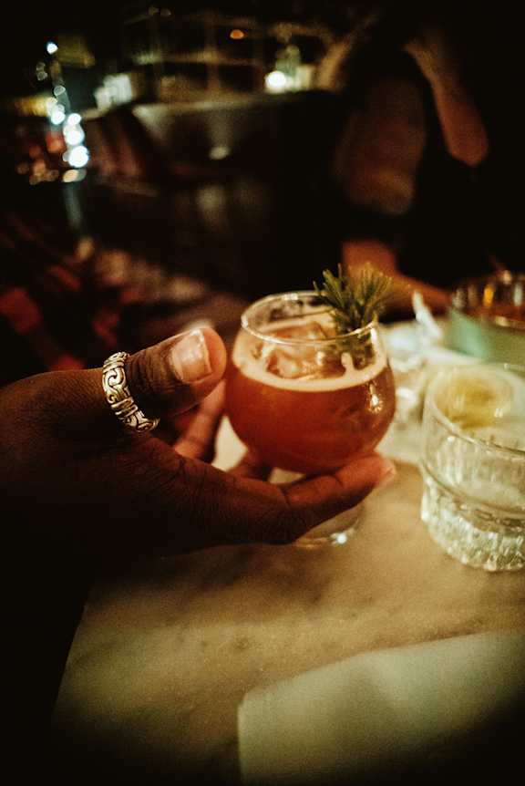 A person holding a glass with a drink and a sprig of rosemary on top. at The Fowler Apartments, Boise, ID