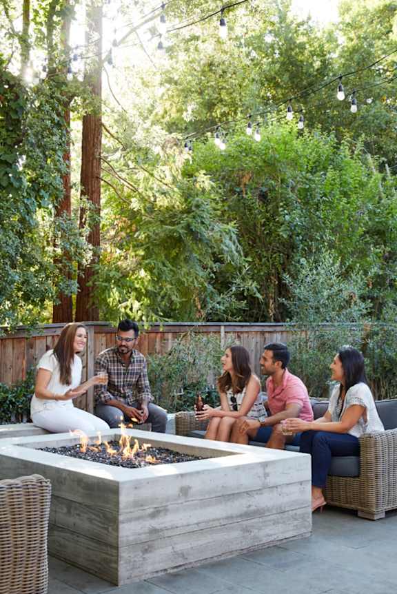 A person is grilling corn on the cob and another person is holding a fork.