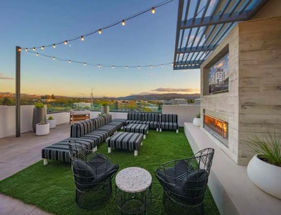 A Rooftop Deck With Lounge Chairs, Fireplace, Wall-Mounted TV, Tables, And City Views. at NoMa Apartments, California, 94596