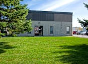Thumbnail 2 of 4 - A building with a grey exterior and a green lawn in front.