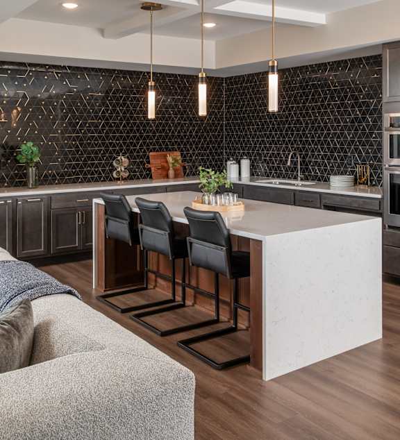 a kitchen with a white island and chairs in front of a black accent wall