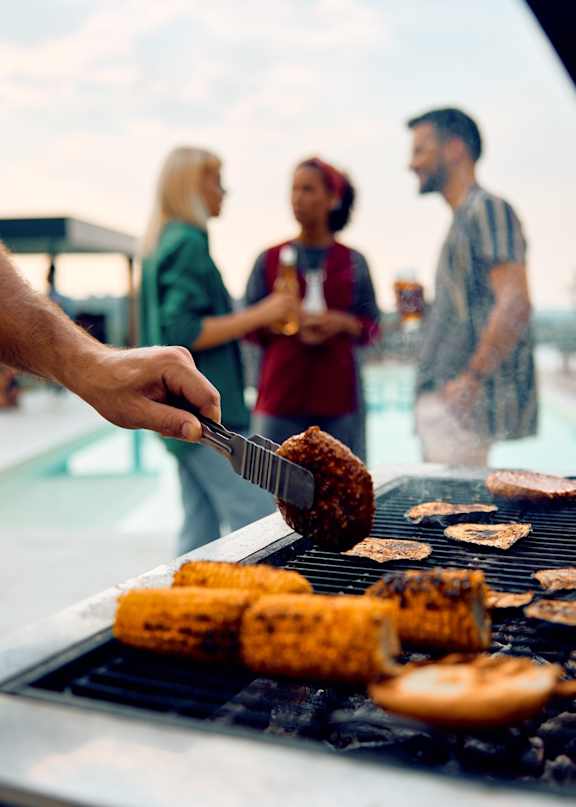 A person is grilling corn on the cob and another person is holding a fork.