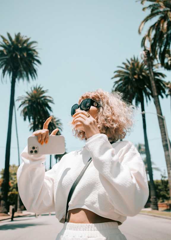 A person with curly hair is taking a selfie with a smartphone.