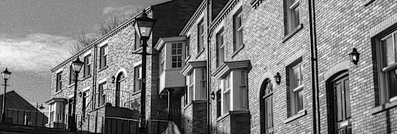 A black and white image of a row of houses with a street lamp in the foreground.