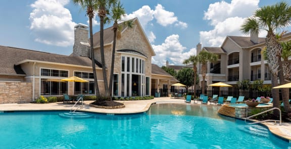 a large swimming pool with lounge chairs and umbrellas in front of a building