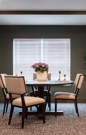 A dining room with a table set for two and a potted plant on the side.
