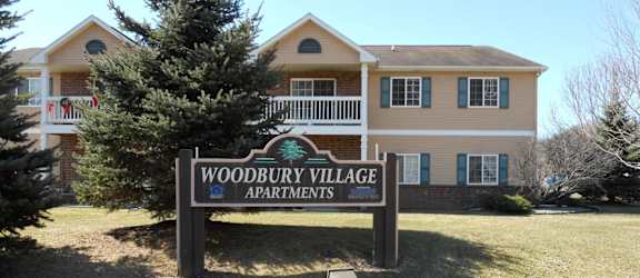 A sign for Woodbury Village Apartments stands in front of a building.