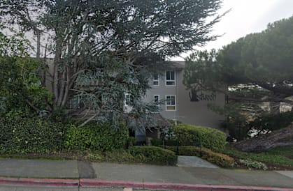 A grey building with trees in front of it.