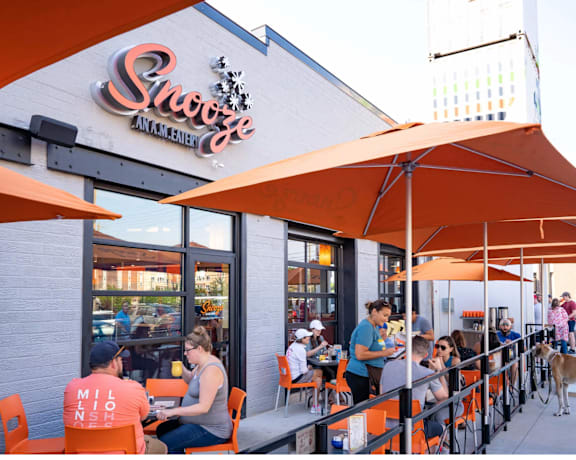 A restaurant with orange umbrellas and people sitting at tables.