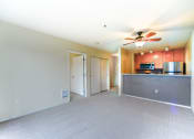 Thumbnail 10 of 22 - A spacious living room with a ceiling fan and a kitchen area in the background.