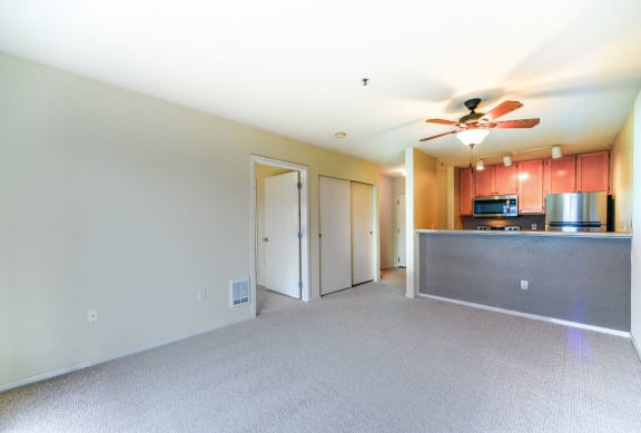 A spacious living room with a ceiling fan and a kitchen area in the background.