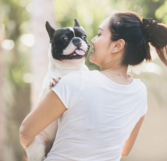 A woman in a white shirt is holding a black and white dog.