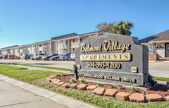 A sign for Belmont Village Apartments is in front of a row of houses.