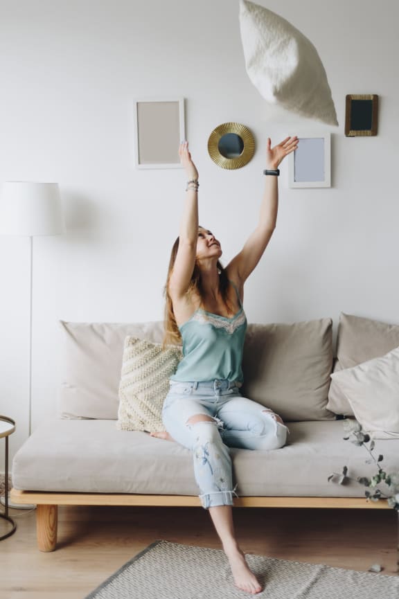 woman throwing pillow in the air sitting on couch