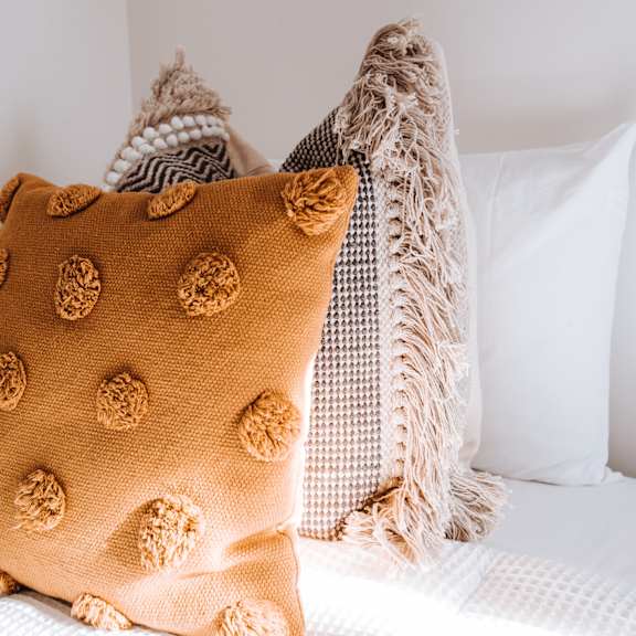 A tan pillow with a pattern of circles is on a bed.