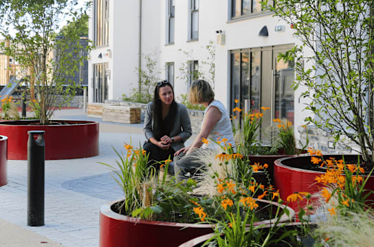 two women talking in a garden on the side of a building