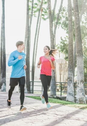 a man and a woman running on a sidewalk with palm trees in the background at Altezza High Desert, New Mexico, 87111