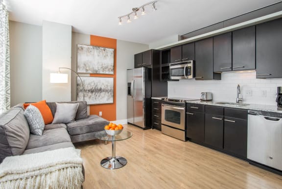 A modern kitchen with a grey couch and orange accents. at Lex and Leo at Waterfront Station, Washington, DC