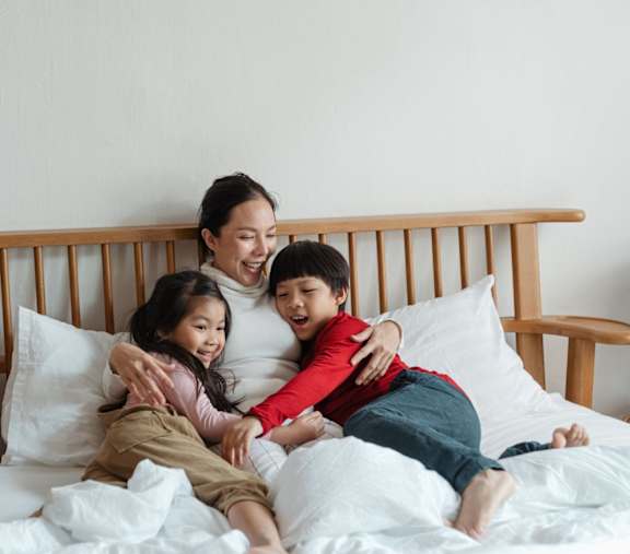 A Woman and Two Children Are Sitting on a Bed at The Westerly at Union Depot Apartments, Bartlett, 38134
