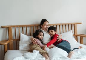 cheerful-ethnic-mother-hugging-children-lying-in-bed at Madison Shelby Farms Apartments, Memphis, TN 38120