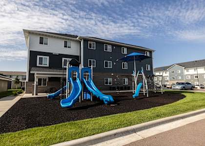 A playground with a blue slide in front of a two-story building.